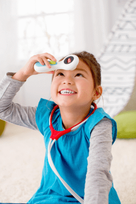 Niña sostiene el termómetro del juguete de doctor Fisher-Price sobre su frente.